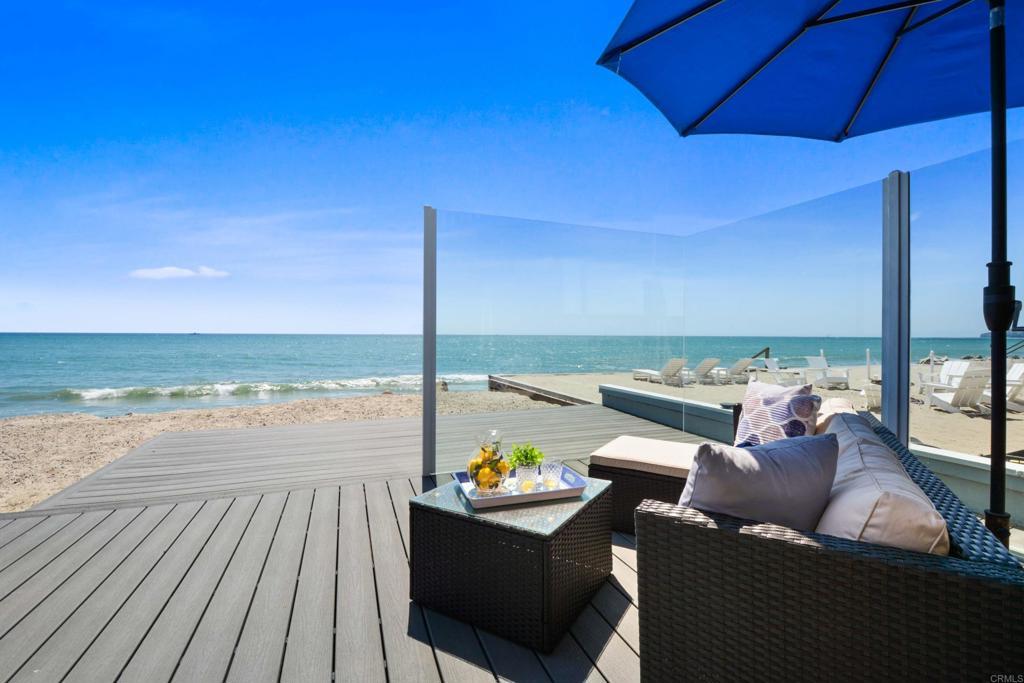 Outdoor seating on a beachfront deck with ocean view and glass windbreak